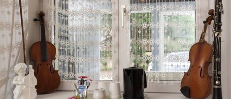 A room with a window adorned with lace curtains, a violin, a cello, a clarinet, and a small statue of a cherub.