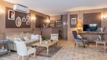 Un salon comprenant un canapé, des fauteuils, une table basse, un téléviseur et un coin bar avec des bouteilles.