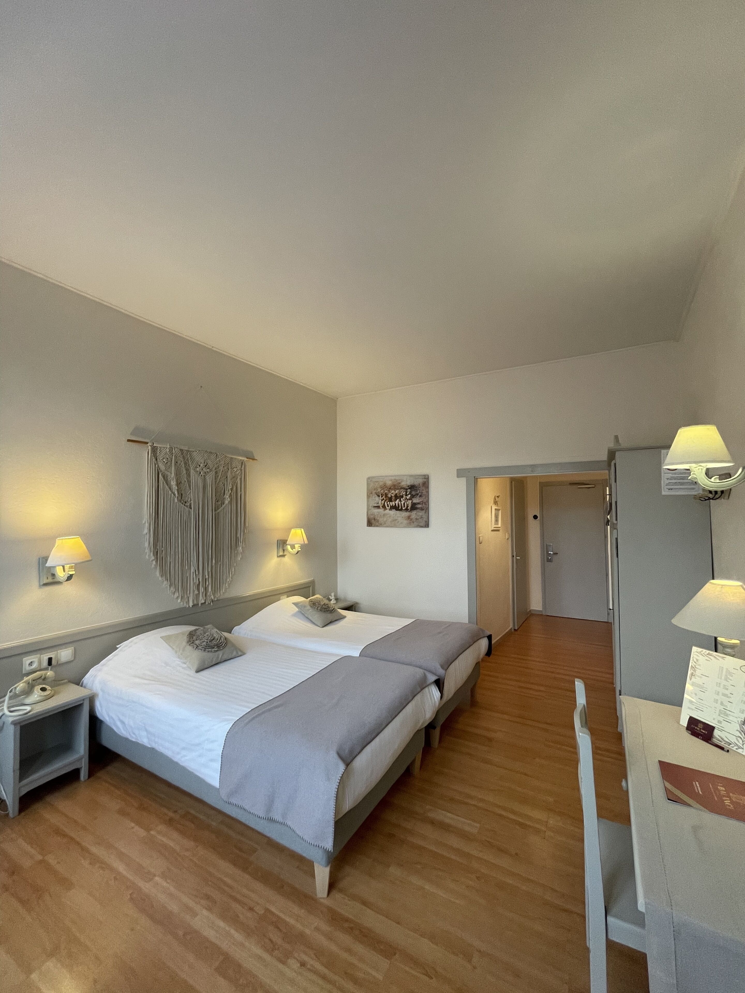 A hotel room with two beds, a desk with a lamp, a telephone, and a door leading to another room.