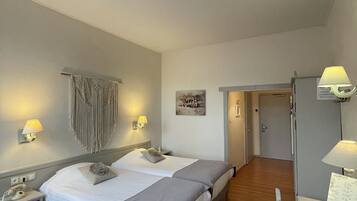 A hotel room with two beds, a desk with a lamp, a telephone, and a door leading to another room.