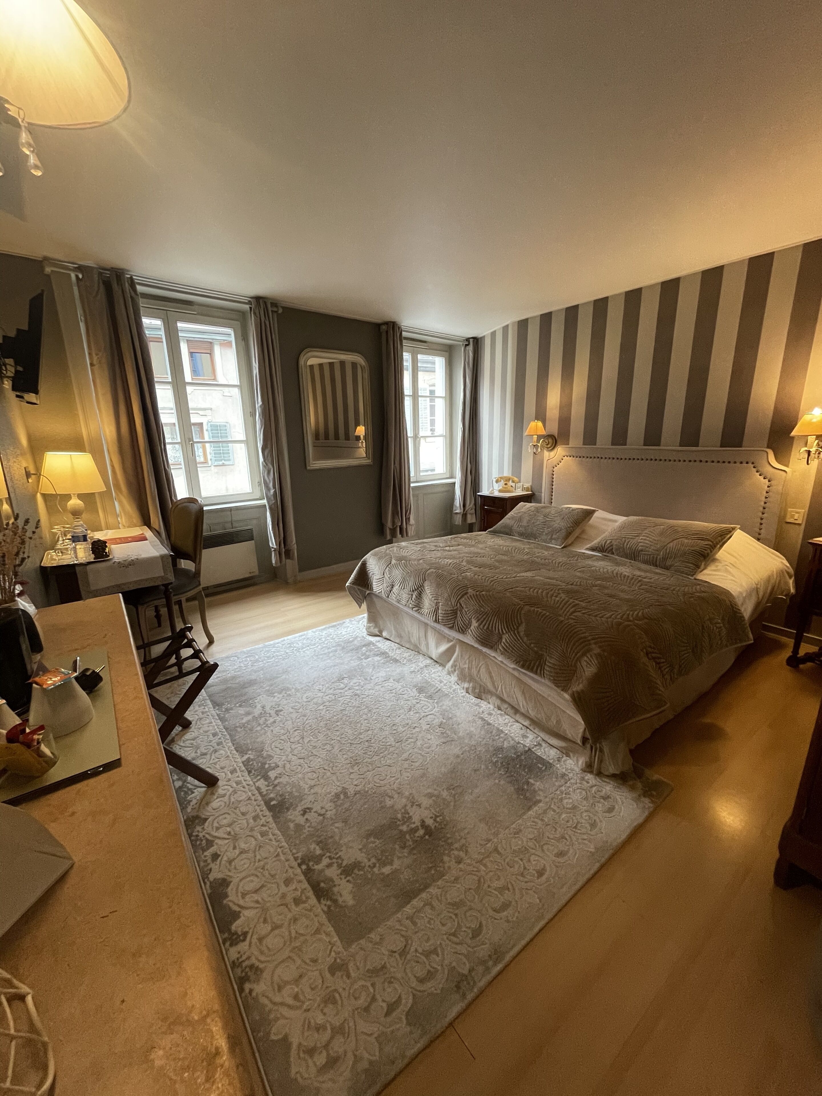 Habitación de hotel con una cama grande, un escritorio con silla, una lámpara y una ventana con cortinas.