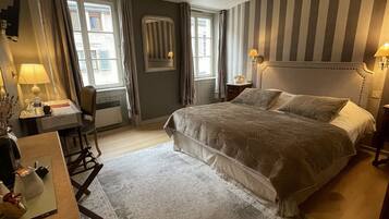 Habitación de hotel con una cama grande, un escritorio con silla, una lámpara y una ventana con cortinas.