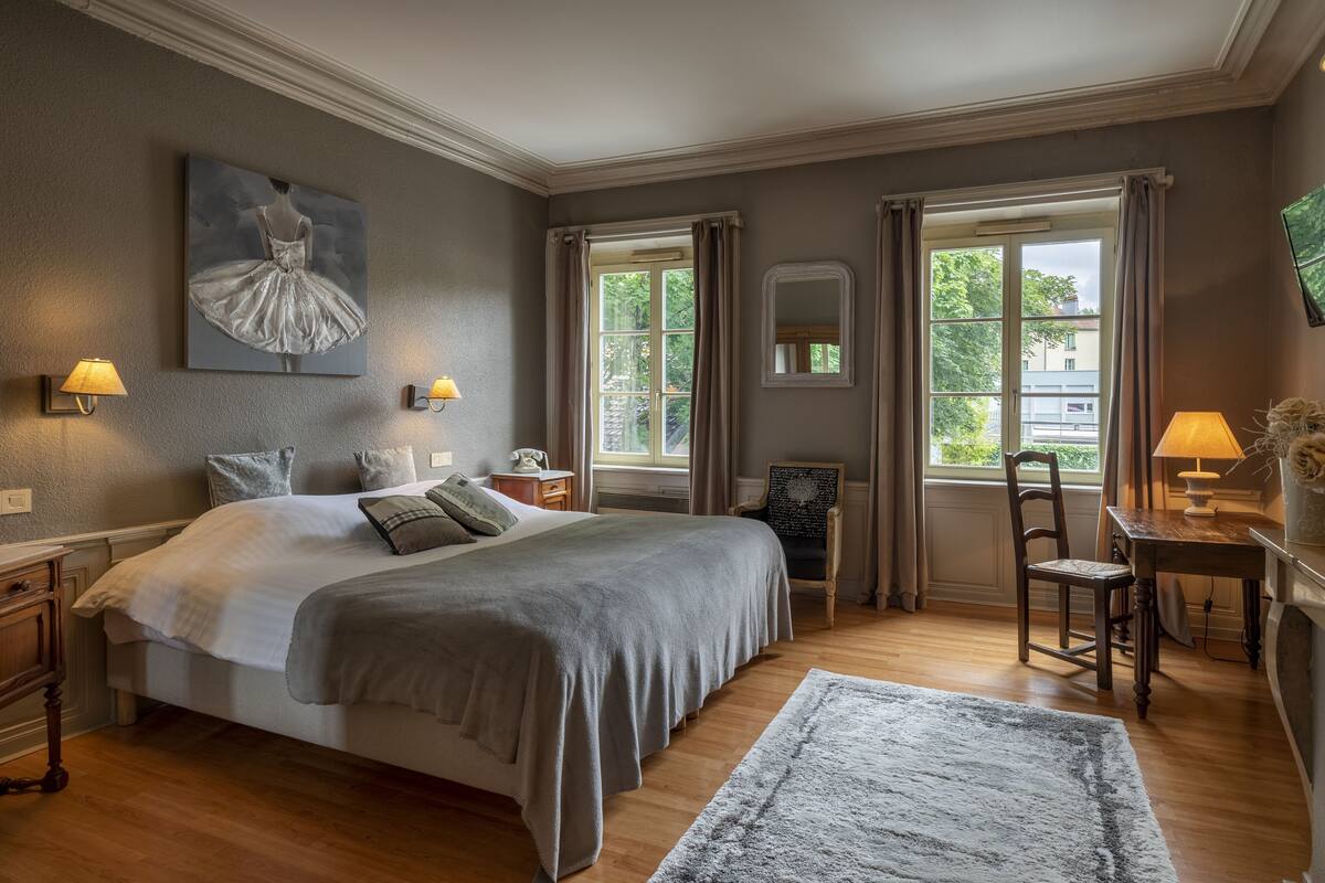 Een slaapkamer met een groot bed, twee nachtkastjes, een stoel, een bureau en een raam met gordijnen.