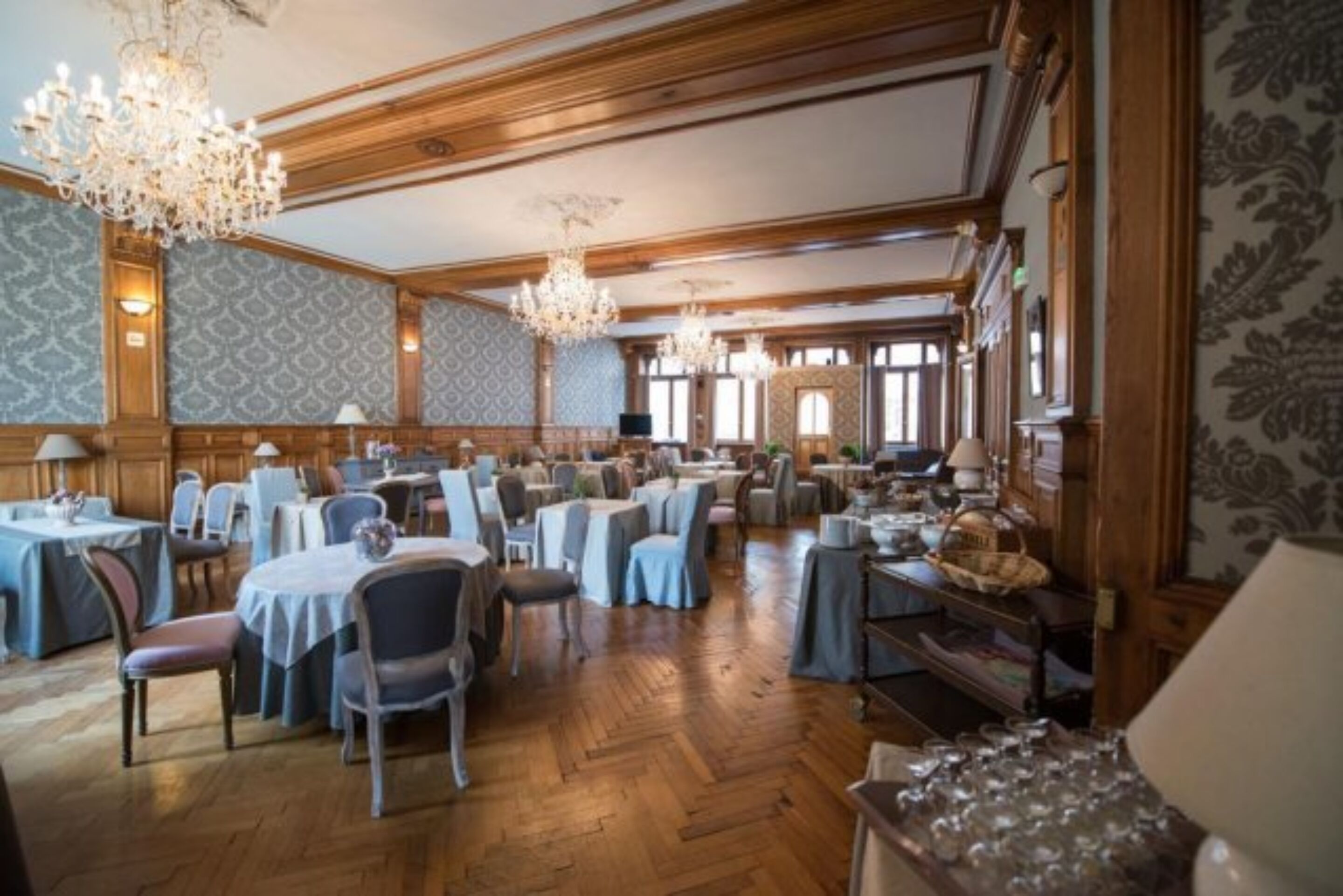 Un amplio comedor con paneles de madera, candelabros y mesas dispuestas para comer.