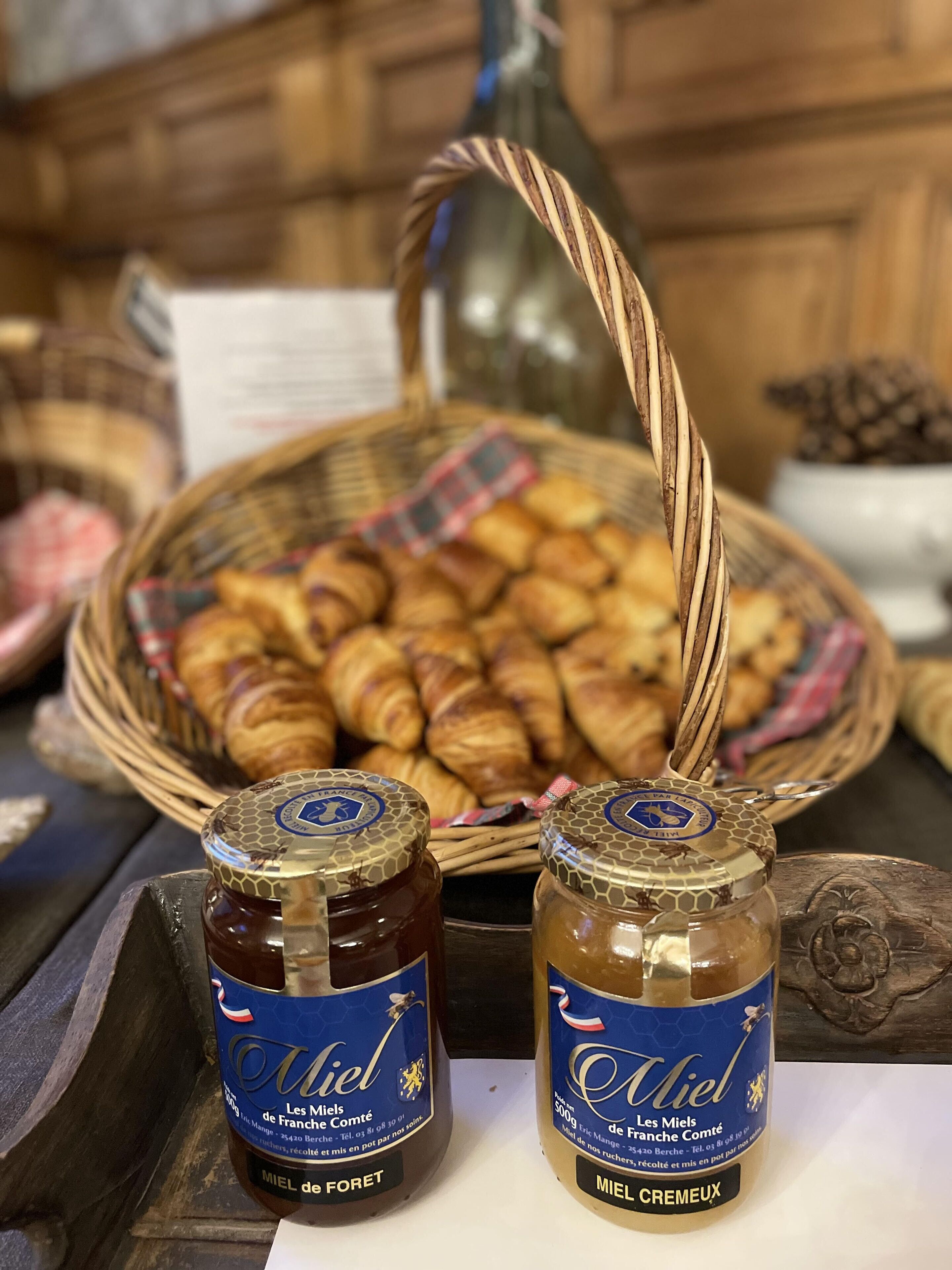 Deux pots de miel et un panier de croissants sur une table en bois.