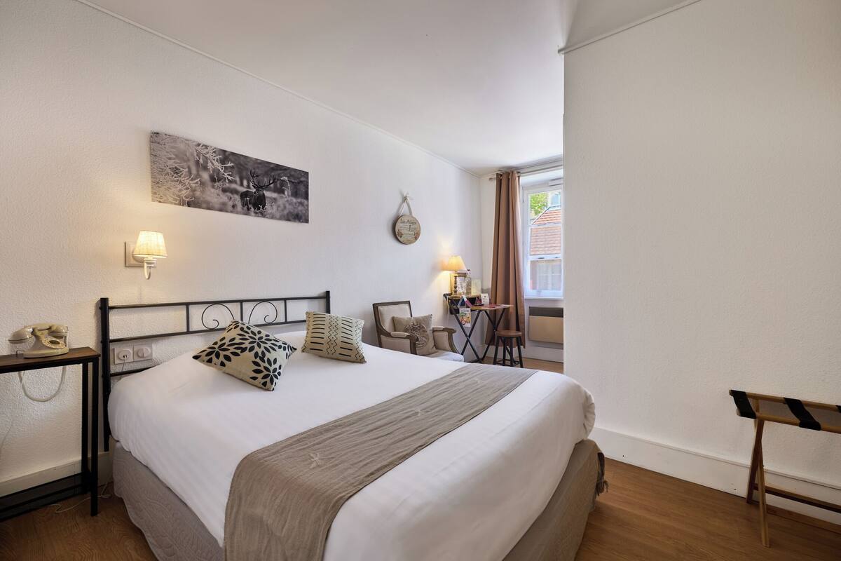 Een netjes ingerichte slaapkamer met een bed, nachtkastjes, een lamp, een stoel en een raam.