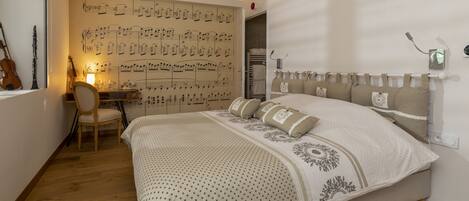 A bedroom with a large bed, a desk with a chair, and a wall with sheet music.