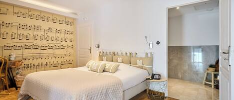 Un dormitorio con una cama grande, una pared decorada con notas musicales, una mesita de noche pequeña y un baño con suelo de mármol.