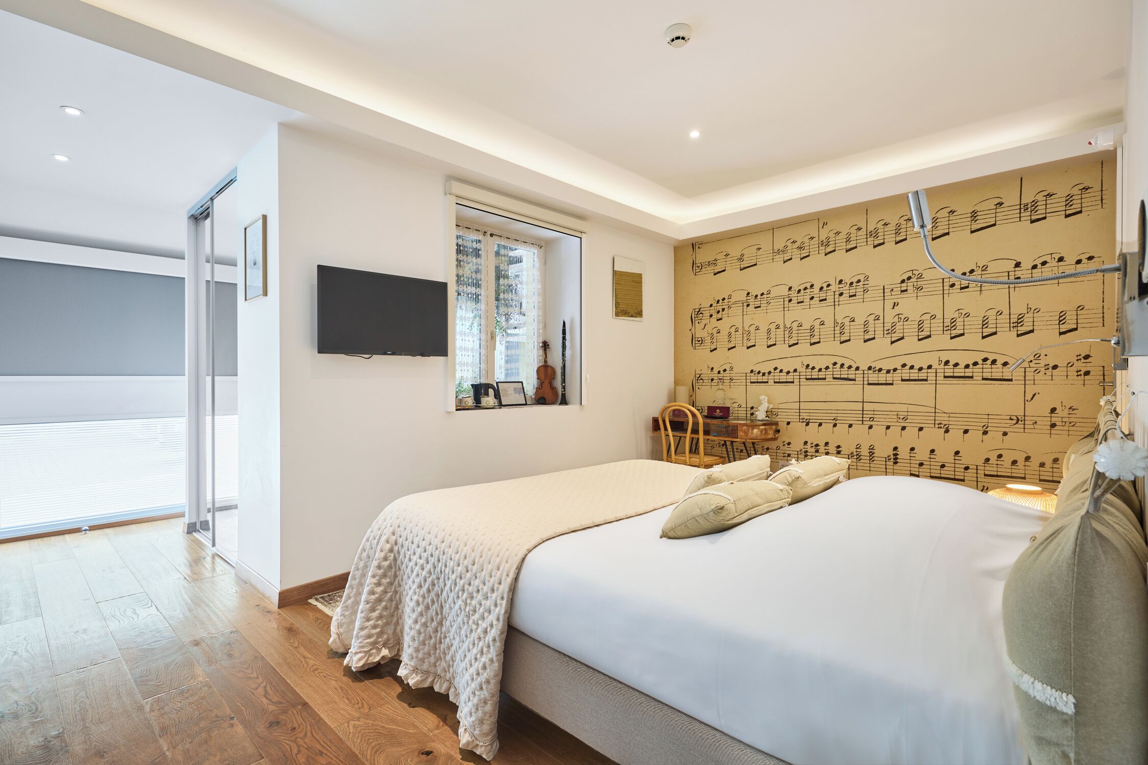 Un dormitorio con una cama grande, televisor montado en la pared y una ventana con cortinas.