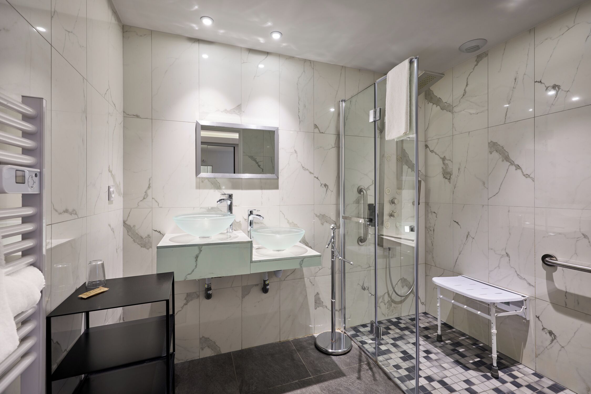 Un baño moderno con paredes de mármol, cabina de ducha de vidrio y tocador con lavamanos blanco.