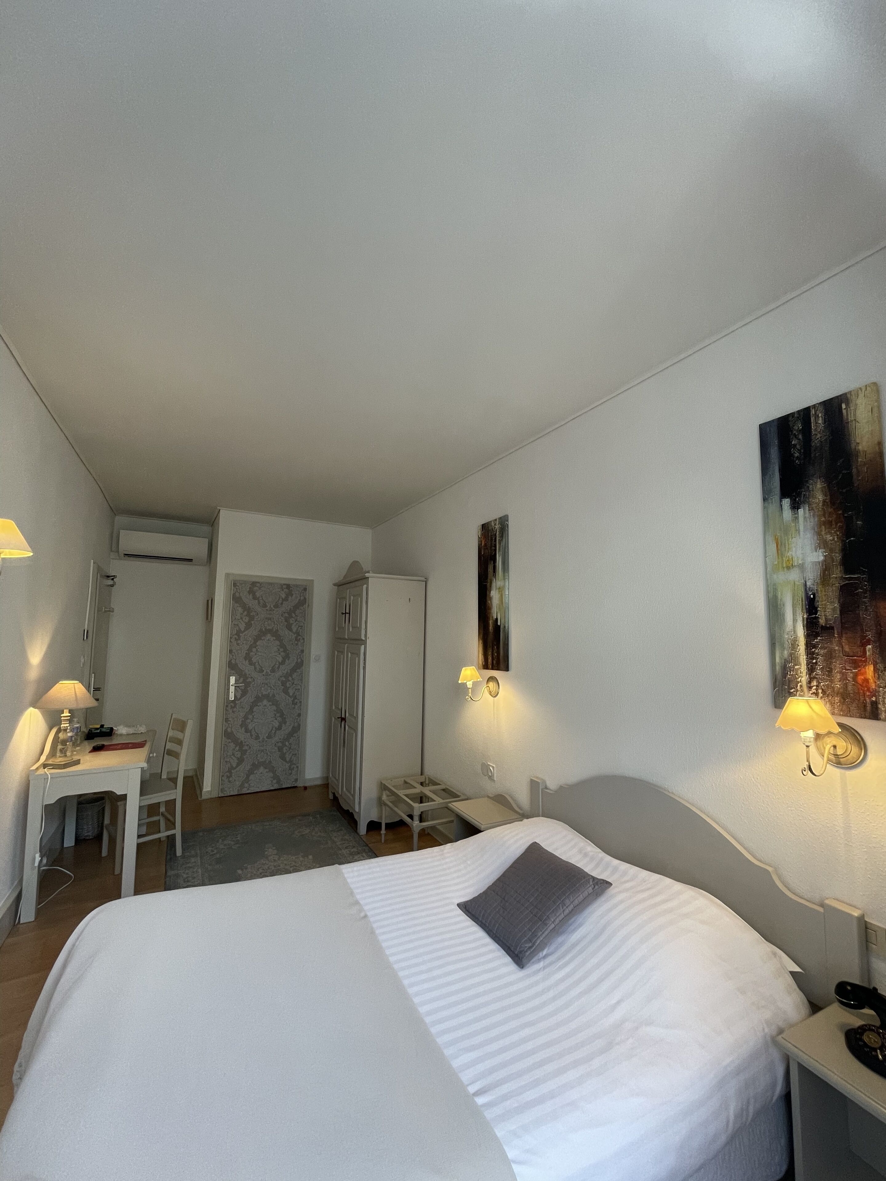 A hotel room with a bed, a desk, a chair, a lamp, and a painting on the wall.