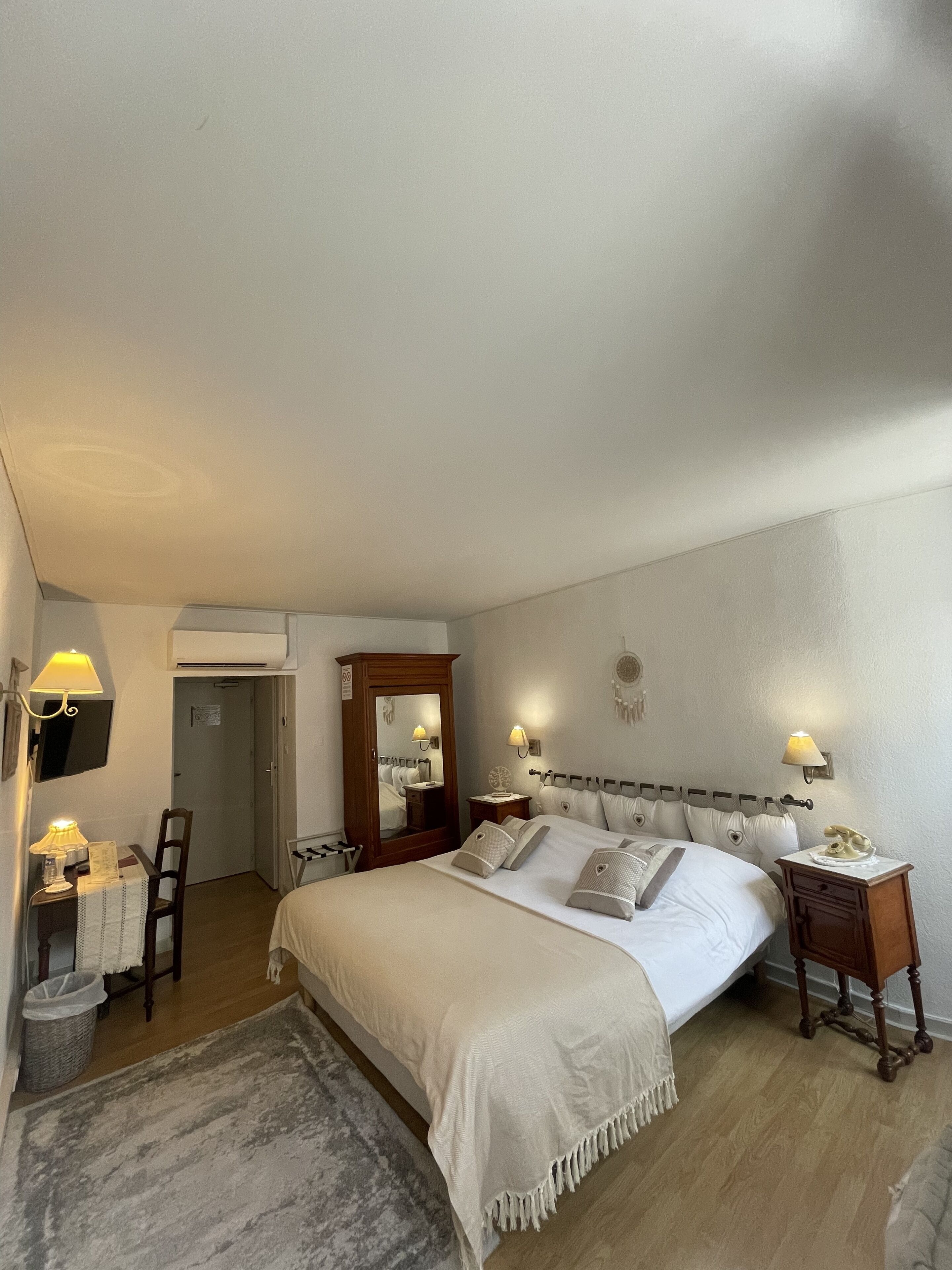 A neatly arranged bedroom with a large bed, bedside tables, a chair, a desk, and a mirror.