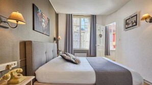 Una habitación de hotel con cama, teléfono, lámpara y ventana con cortinas.
