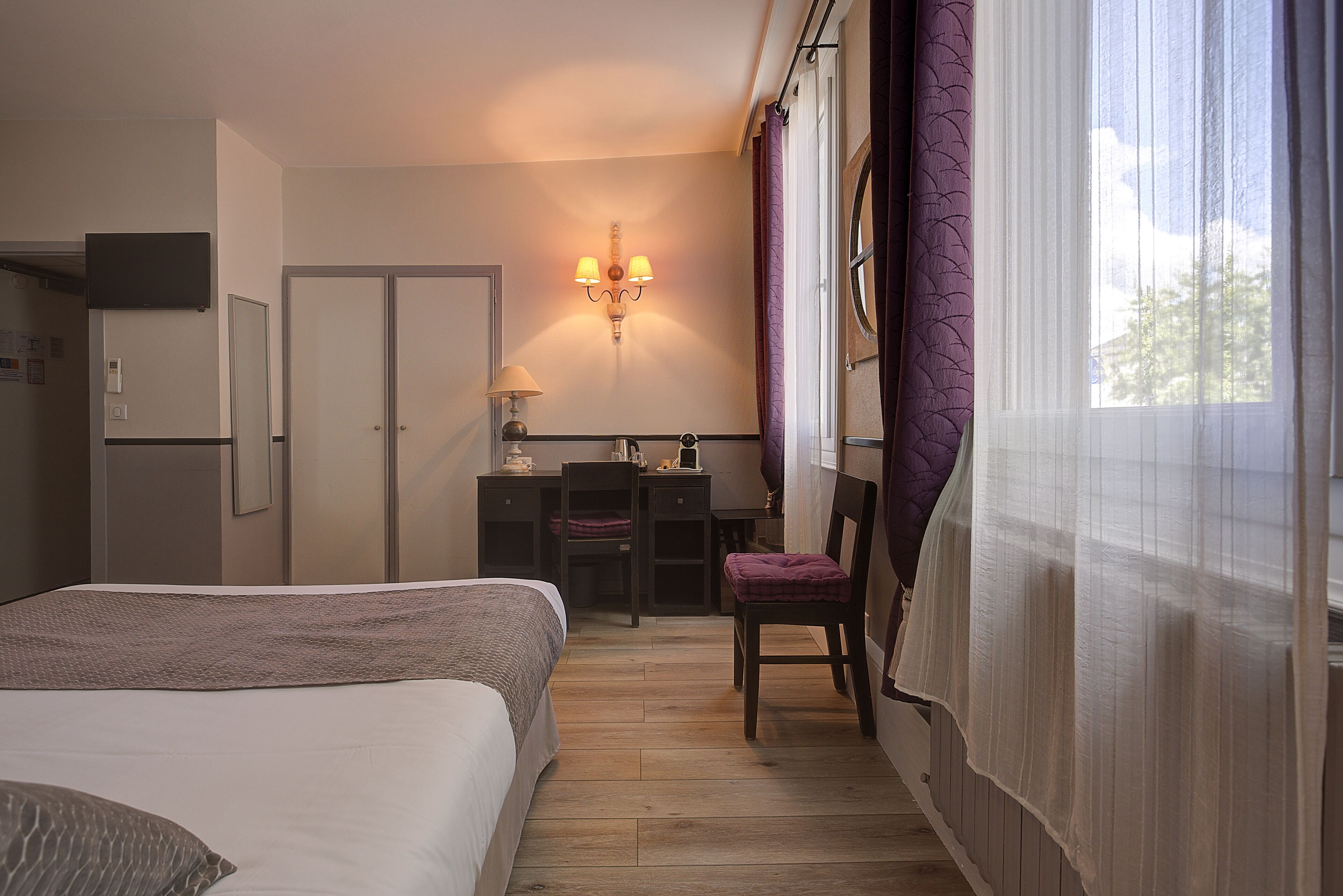 Een hotelkamer met een bed, een bureau, een stoel, een kledingkast en een raam met gordijnen.