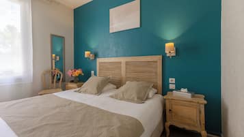 Una cama bien tendida con cabecera de madera, dos mesitas de noche con lámparas, un espejo y un aplique en la pared.