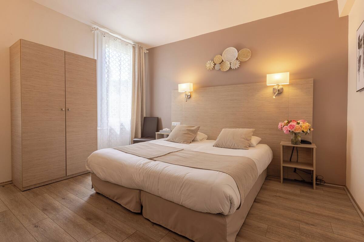 A bedroom with a large bed, two bedside lamps, a nightstand with a vase of flowers, and a wardrobe.