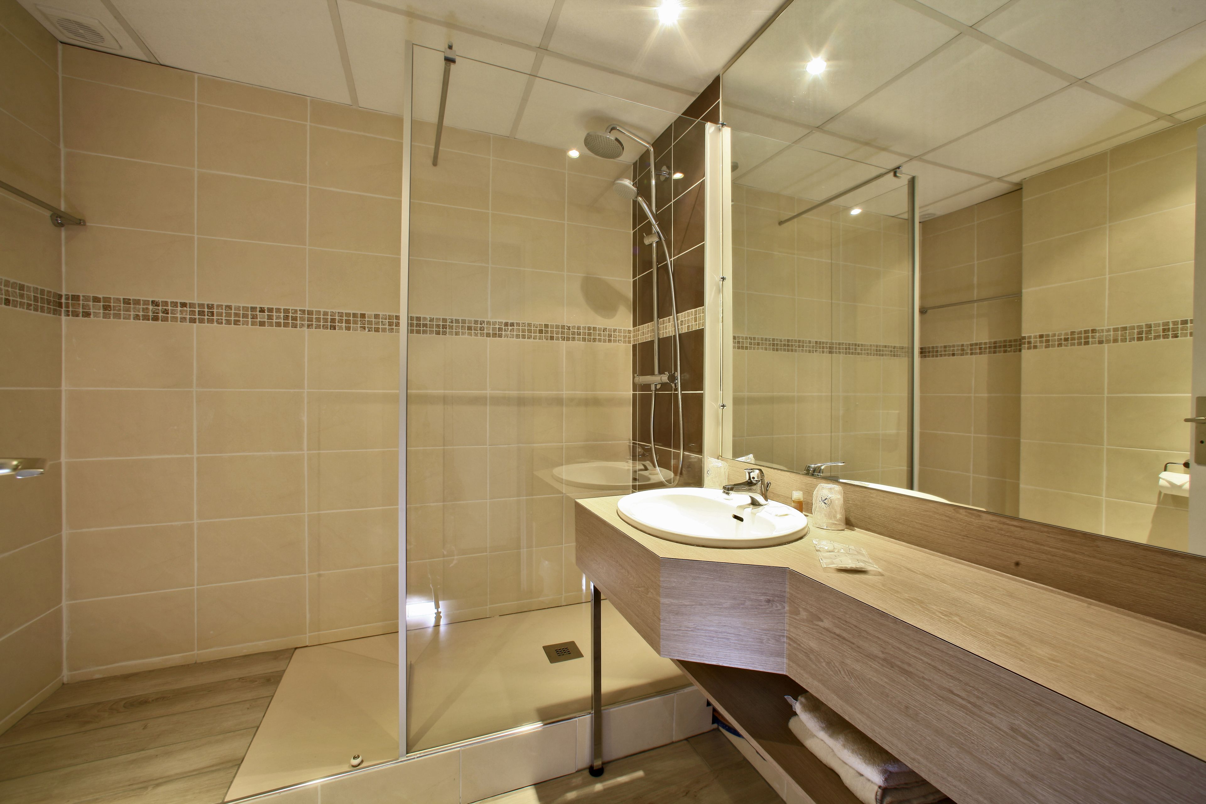 A modern bathroom with a glass shower enclosure, a wooden vanity, and a large mirror.