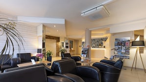 A modern hotel lobby with leather seating, a reception desk, and a magazine rack.