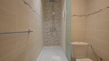 A narrow shower with a glass partition, a toilet, and a towel on the floor.