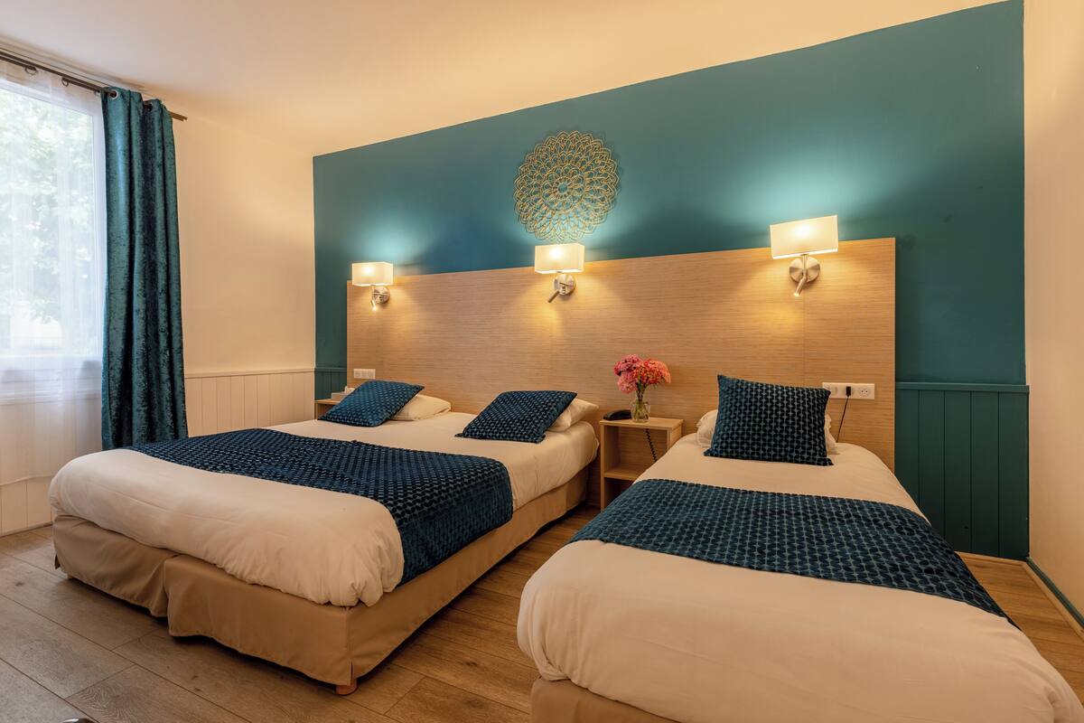 A hotel room with two beds, a wooden headboard, wall-mounted lights, and a decorative wall piece.