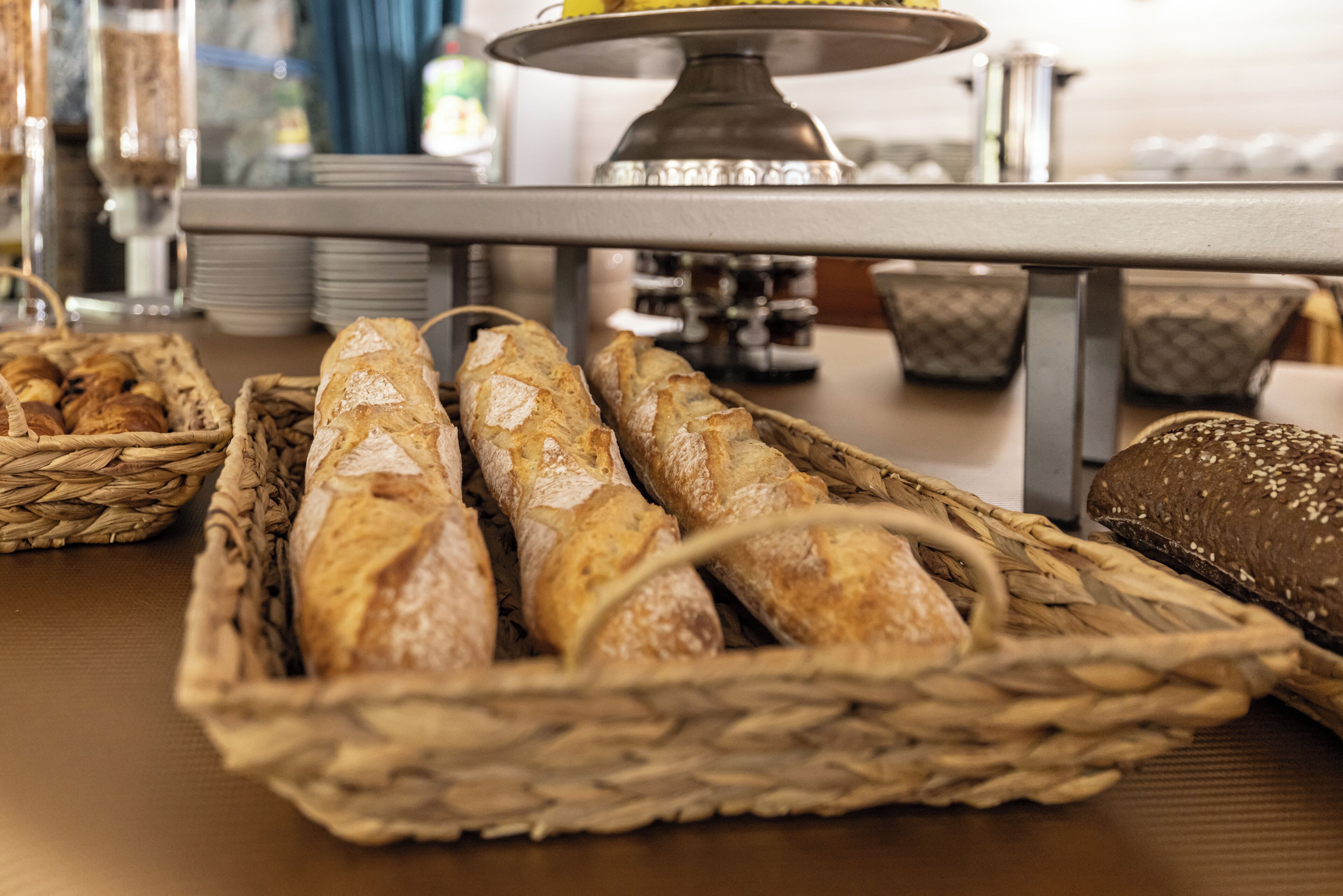 A table with baskets of baguettes and a cake stand in the background.