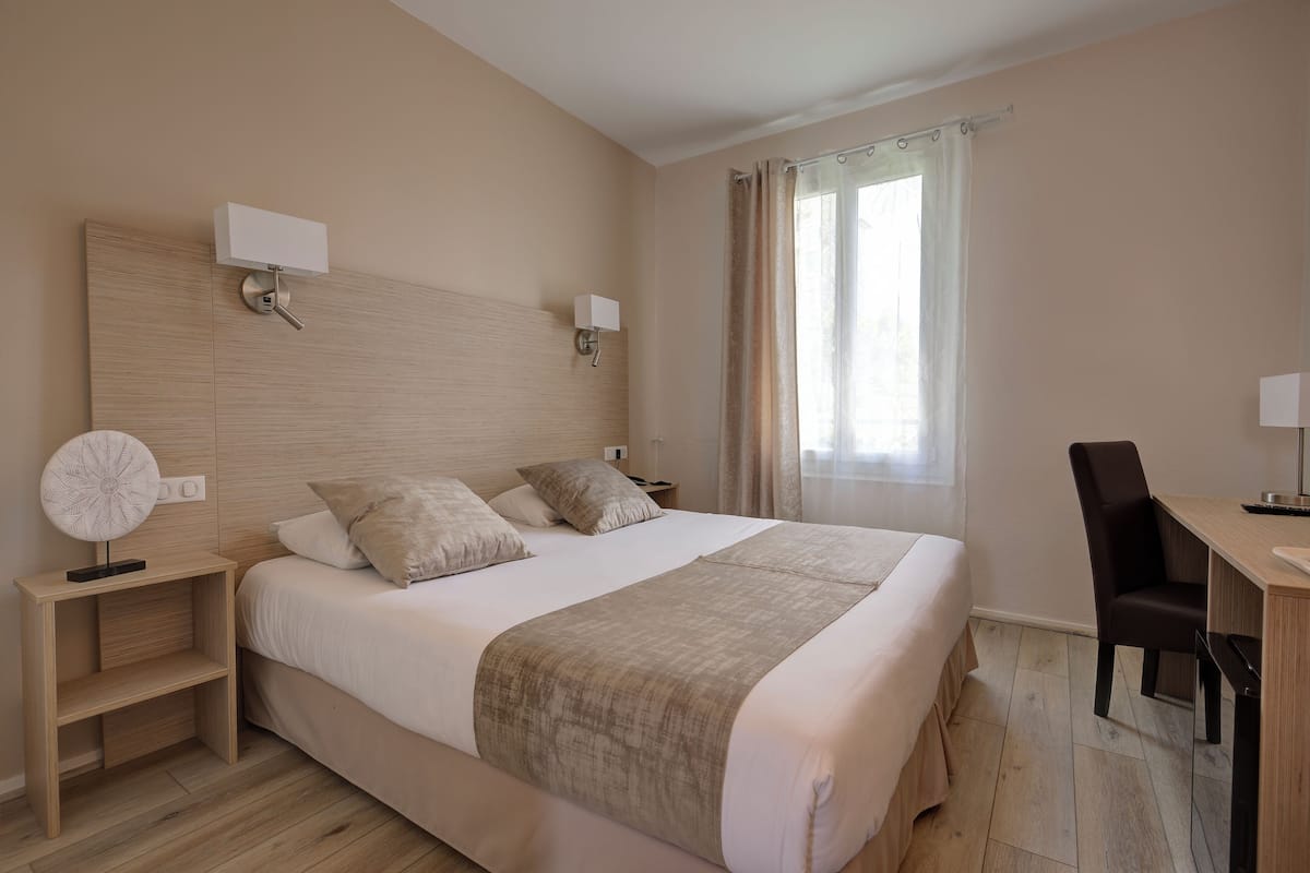 A neatly arranged hotel room with a large bed, bedside tables, a desk, and a chair.