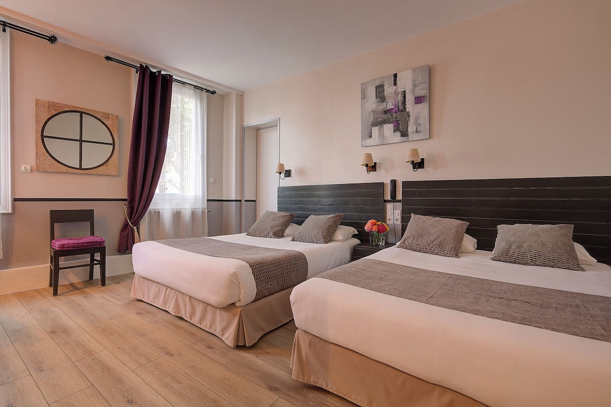A hotel room with two beds, a chair, a window with curtains, a wall clock, and a painting.