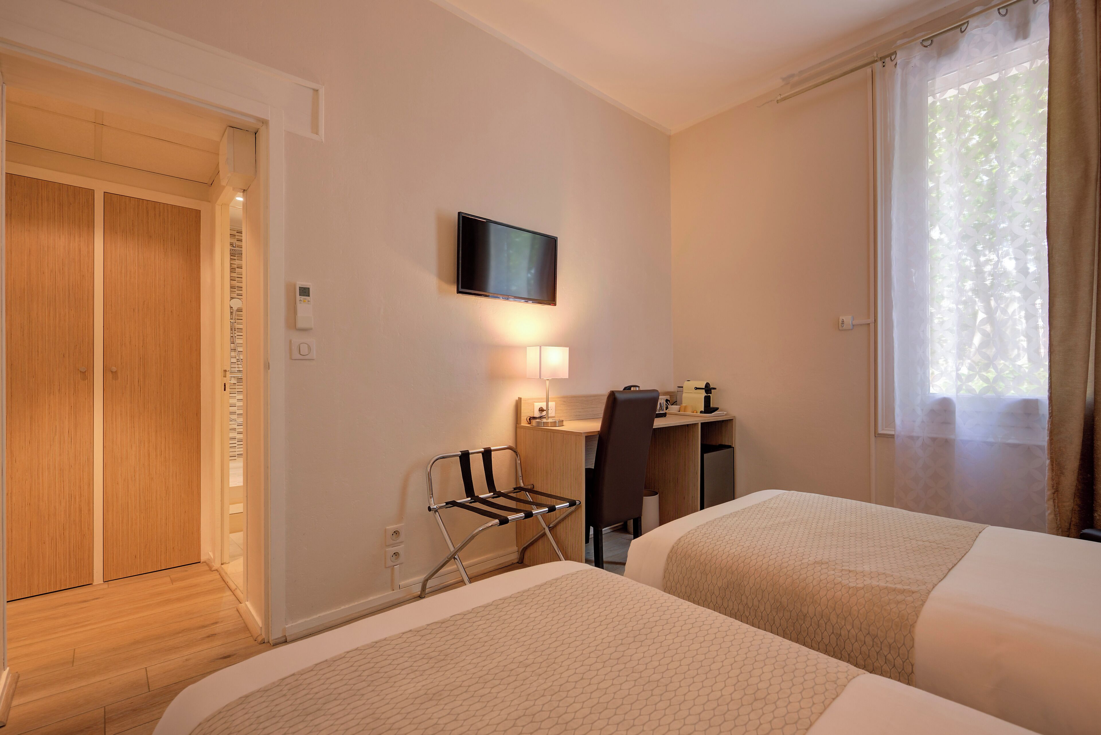 A hotel room with two beds, a desk, a chair, a television, and a window with curtains.