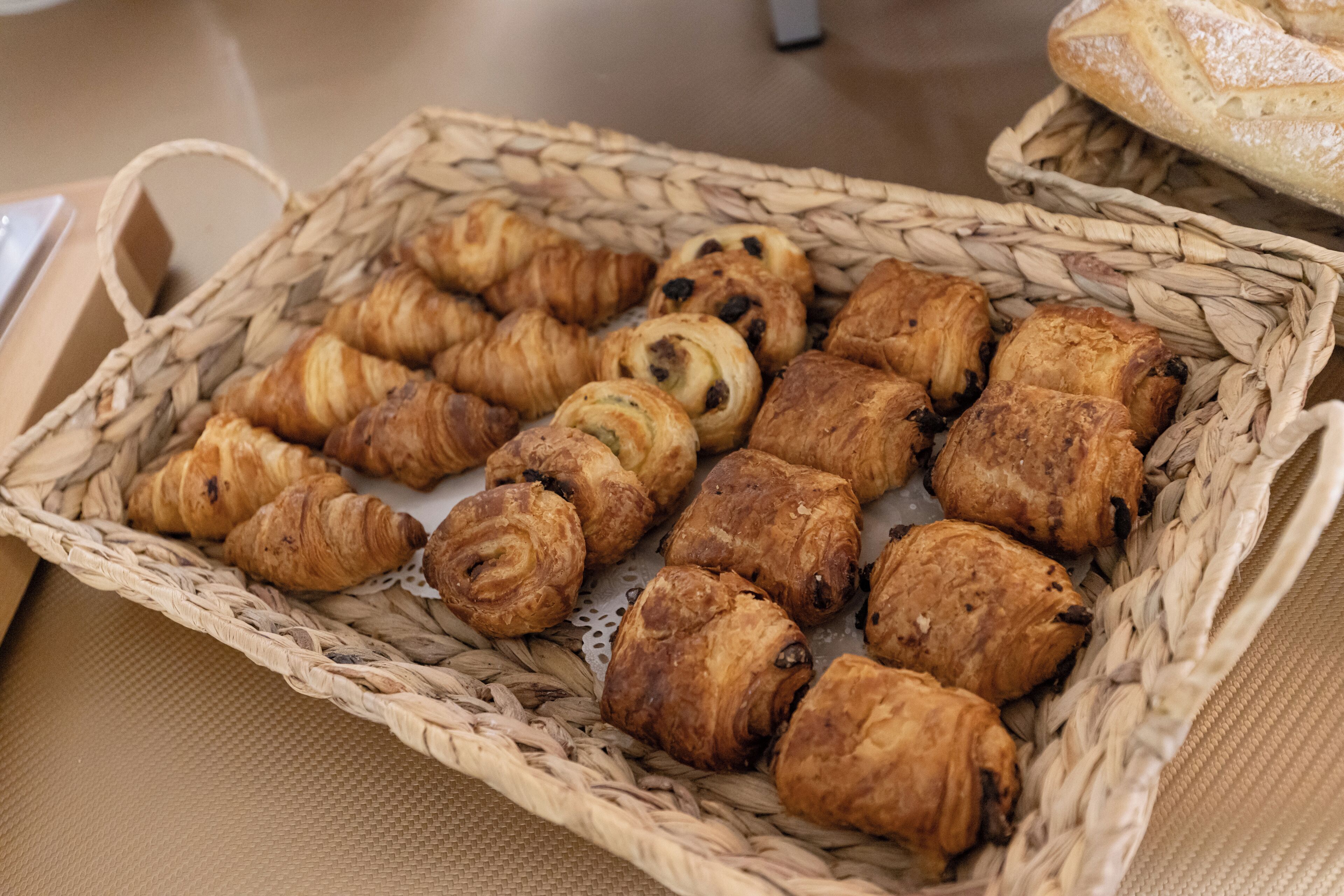 Una cesta con varios pasteles, incluyendo cruasanes y bollos de chocolate, sobre una mesa.