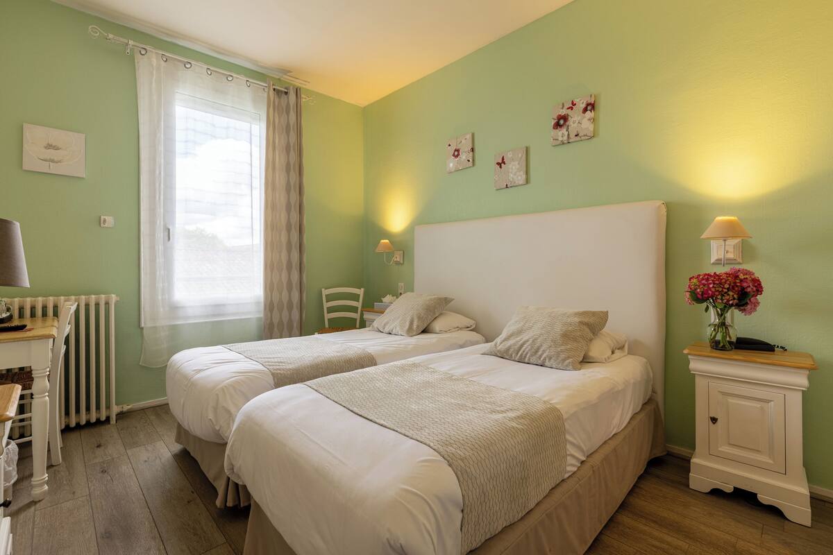 A room with two beds, a desk, a chair, a radiator, and a window with curtains.