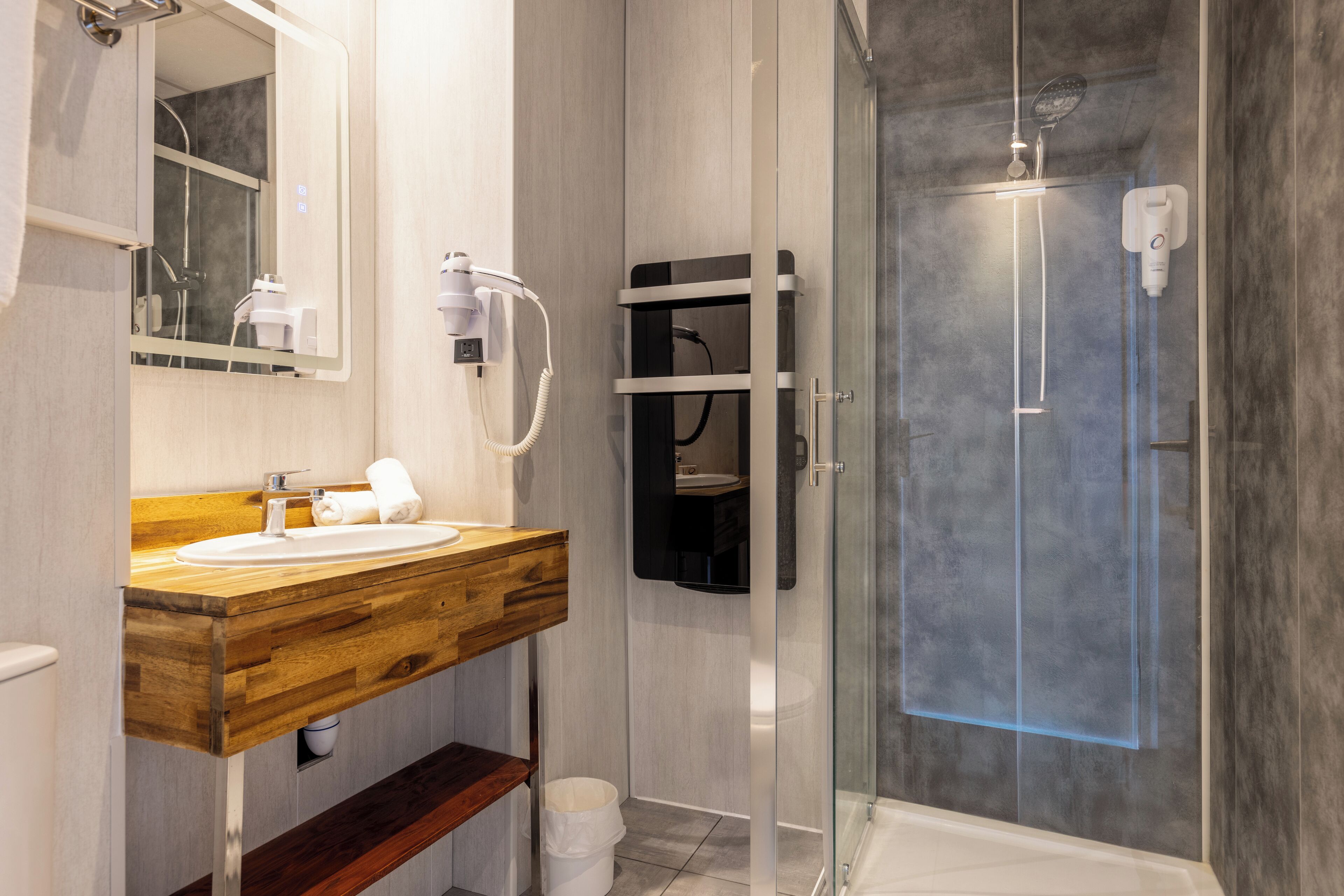 Un baño moderno con tocador de madera, cabina de ducha con mampara de vidrio y espejo empotrado.