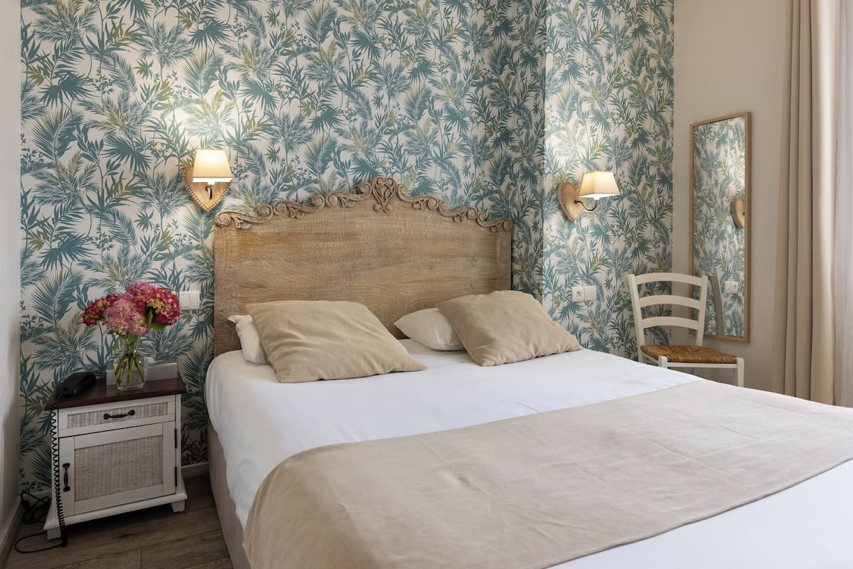 A neatly made bed with a wooden headboard, two bedside lamps, a small bedside table with a telephone, and a chair with a cushion.