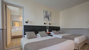 A hotel room with two beds, a large mirror, a wall-mounted artwork, and a nightstand with a lamp.
