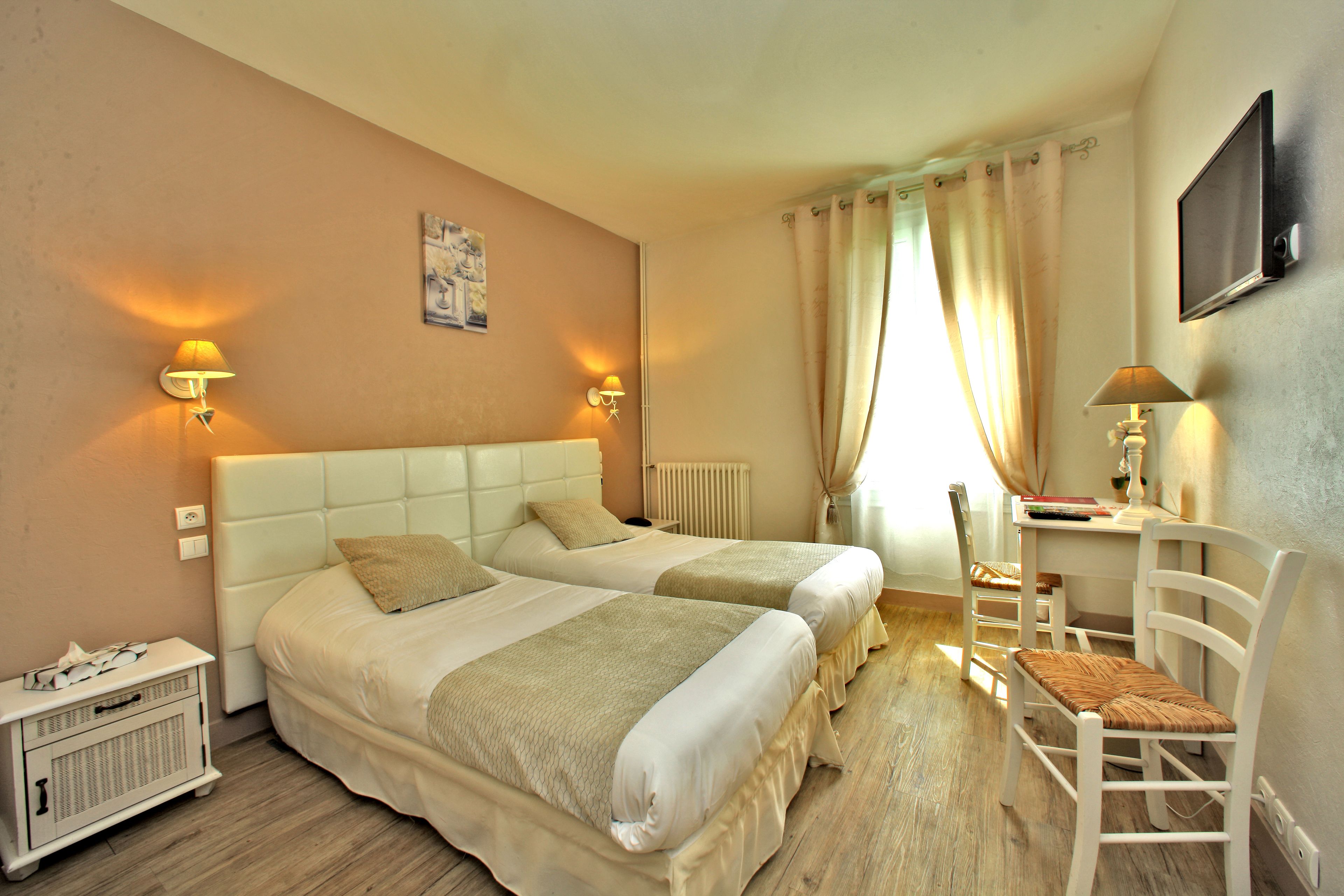 Une chambre d’hôtel avec deux lits, un bureau, une chaise et un radiateur.