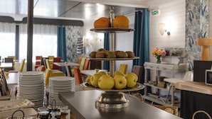 A buffet setup with a three-tiered fruit and cheese board, stacked plates, and condiments.