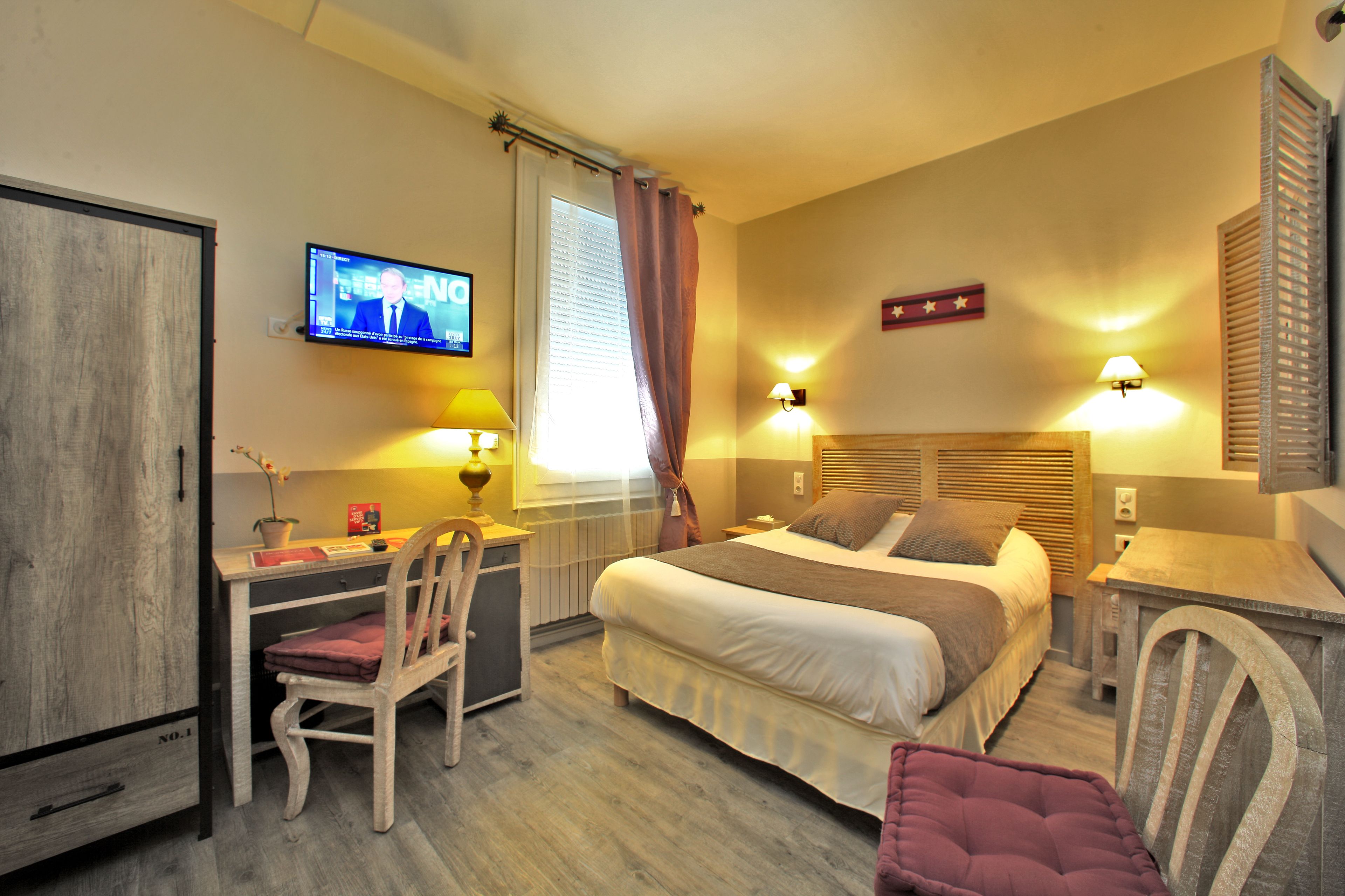 A bedroom with a bed, desk, chair, TV, and lamps.