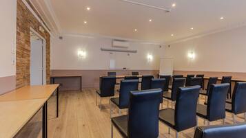 A conference room with a long table and rows of chairs, a whiteboard, and an air conditioning unit on the wall.