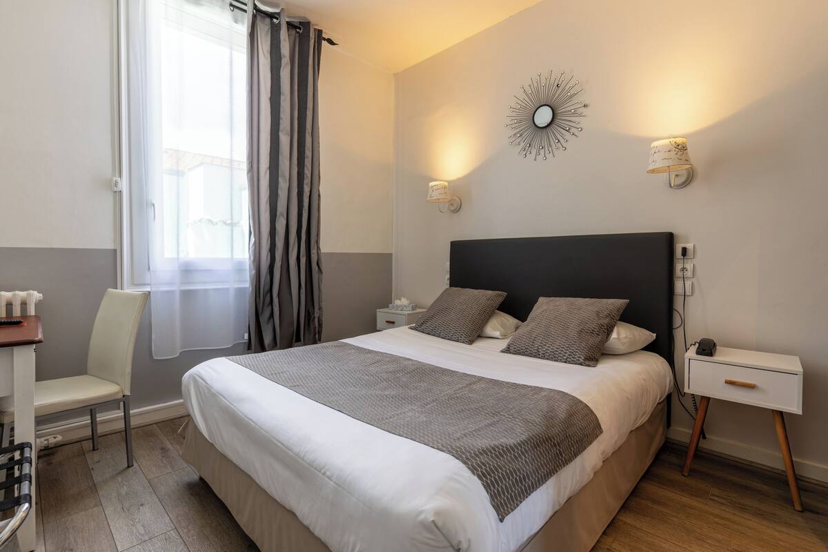 A neatly arranged bedroom with a large bed, bedside tables, a chair, and a window with curtains.
