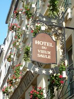 Un letrero de hotel con el nombre "HOTEL DU VIEUX SAULE" y elementos decorativos como estrellas y flores.