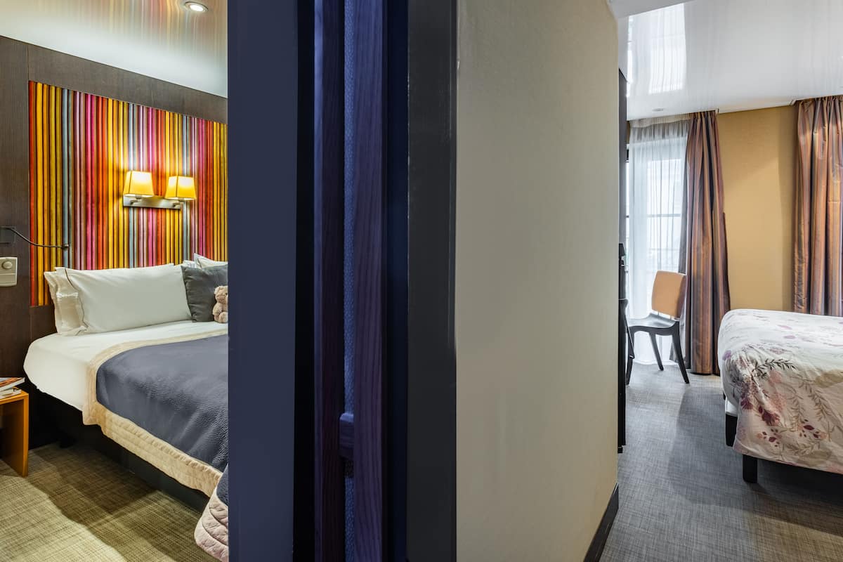 Une chambre d’hôtel avec deux lits, une lampe fixée au mur, une chaise et une vue sur l’extérieur par la fenêtre.