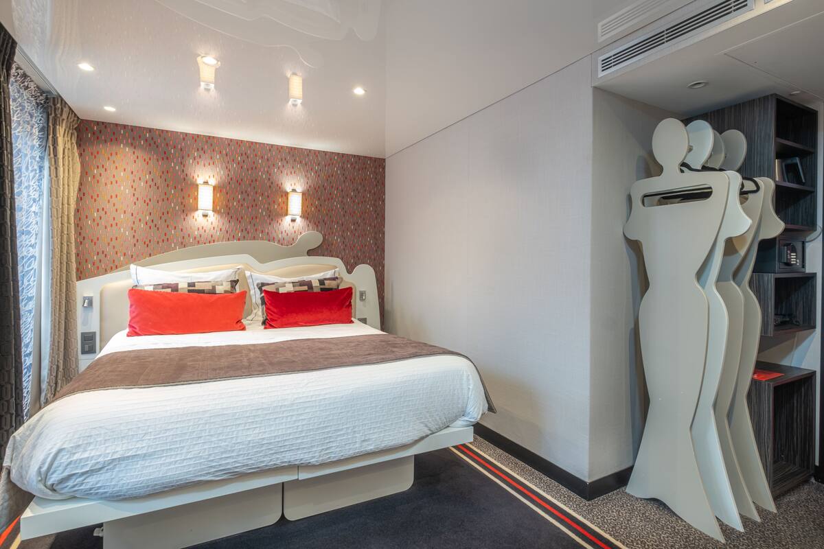 Une chambre d’hôtel moderne dotée d’un grand lit, de deux tables de chevet, d’une petite table, d’une lampe fixée au mur et d’une décoration murale originale.