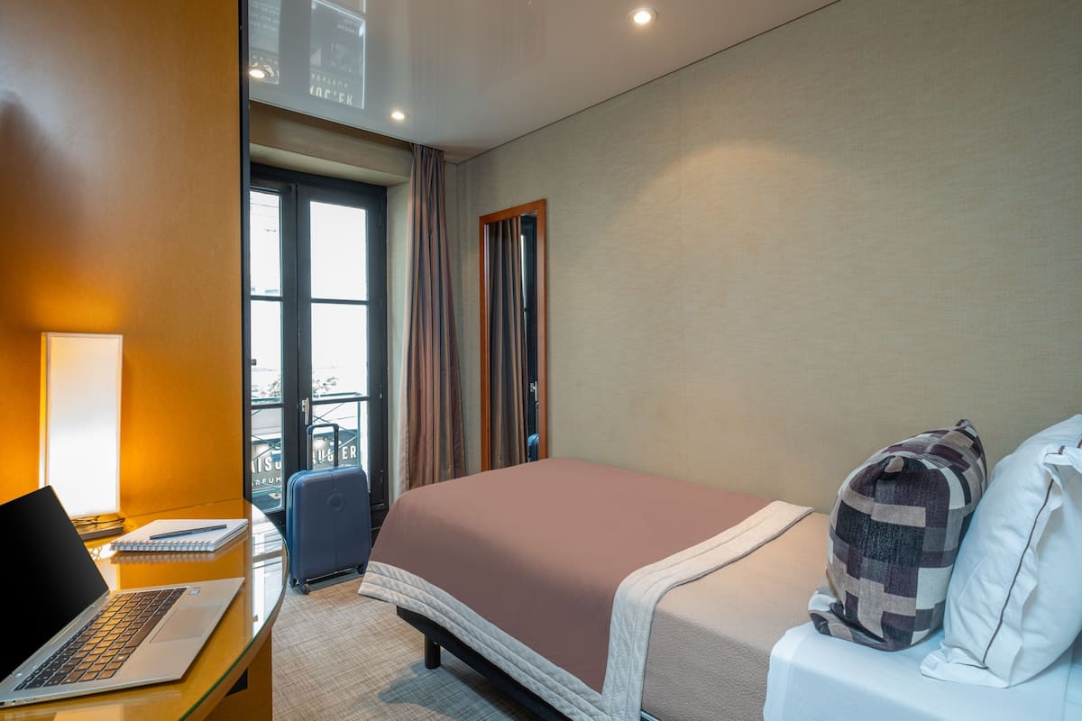 Une chambre d’hôtel avec un lit, un bureau avec un ordinateur portable, une valise et une fenêtre avec des rideaux.