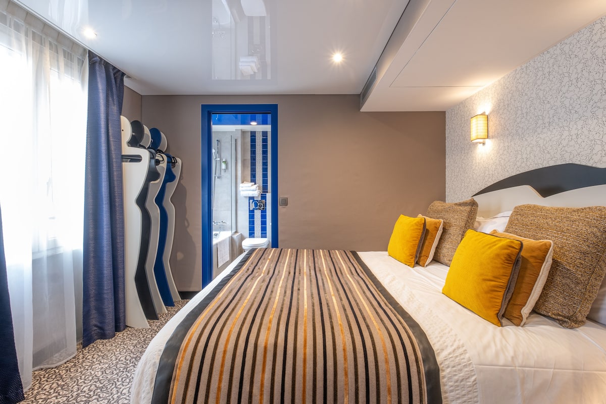 Une chambre d’hôtel avec un grand lit, une salle de bain visible à travers une porte et une moquette à motifs.