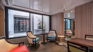 Een moderne hotelkamer met een groot raam, een zithoek met een tafel en stoelen, en een loungehoek met een bank en fauteuils.