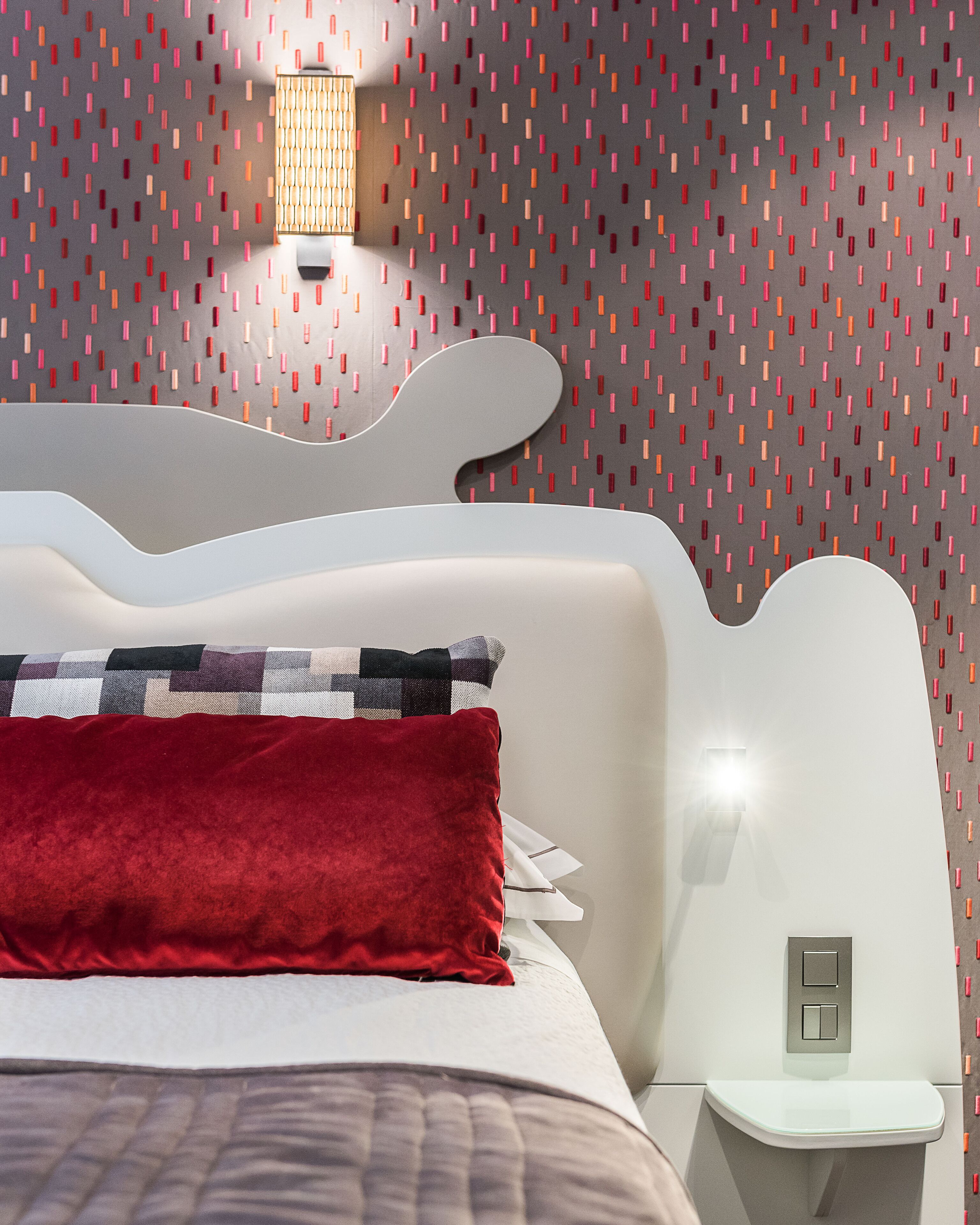 Un dormitorio moderno con una cama blanca, un cojín rojo y una pared con estampado.
