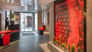 Een moderne lobby met een receptiebalie, zithoek en een grote rode wand met cirkelvormige patronen.