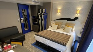 Een moderne hotelkamer met een groot bed, een bureau met een lamp, een stoel en een garderobe.