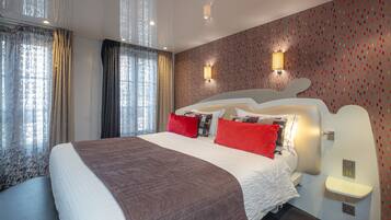 A modern hotel room with a large bed, two bedside tables, a nightstand, and a wall-mounted lamp.