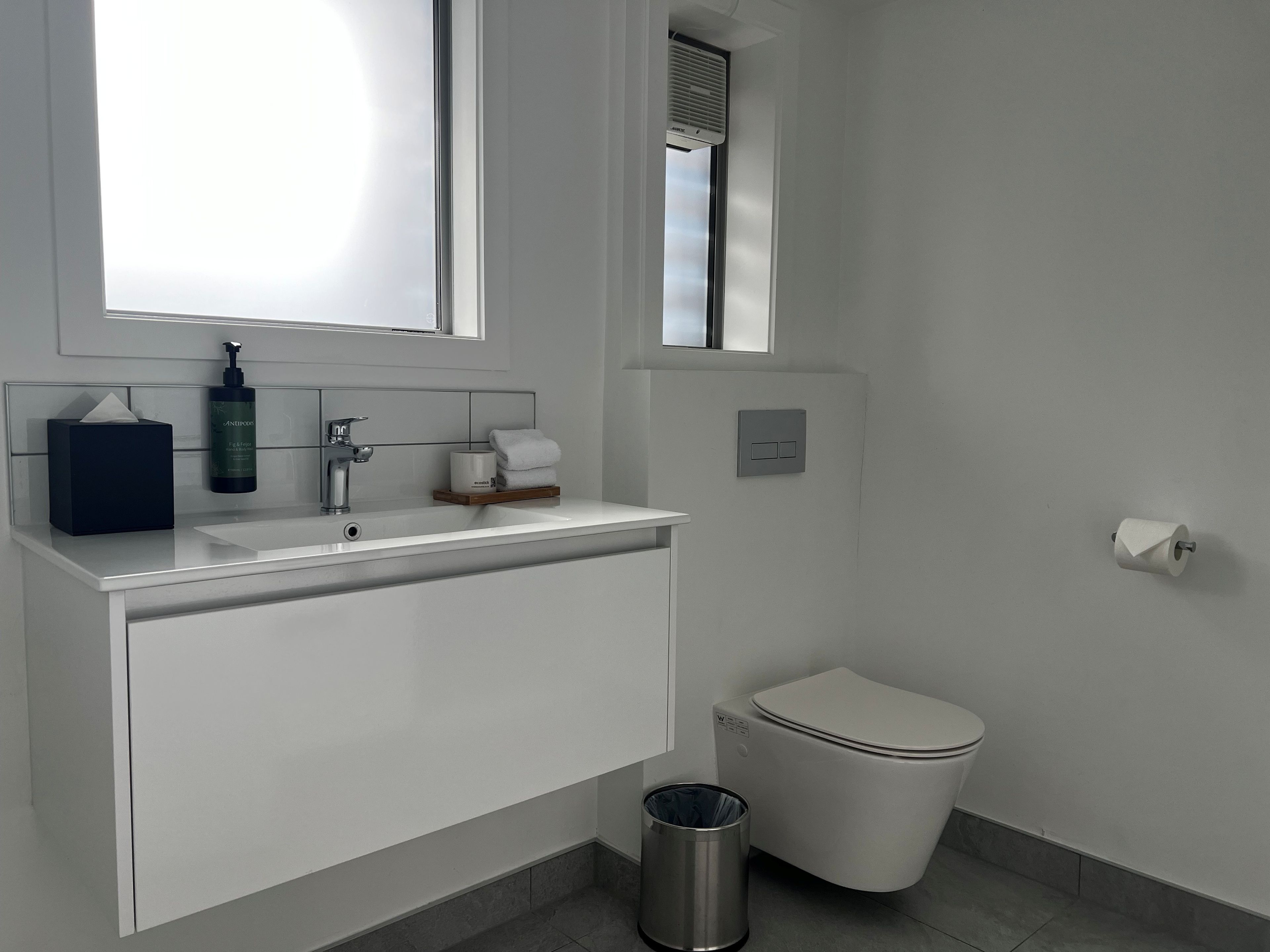 Casa de banho moderna com lavatório branco, espelho, toalheiro, sanita e um contentor de lixo.