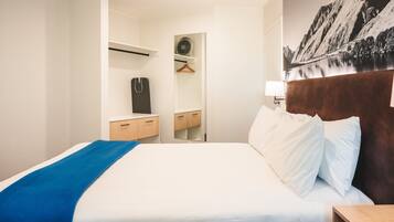 A hotel room with a neatly made bed, a wooden nightstand, a dresser, and a mirror.